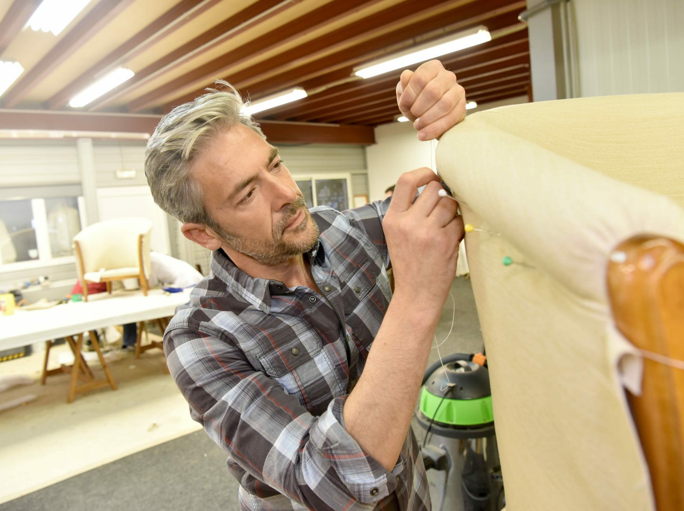 Mann im karierten Hemd polstert ein Sofa mit hellem Leder